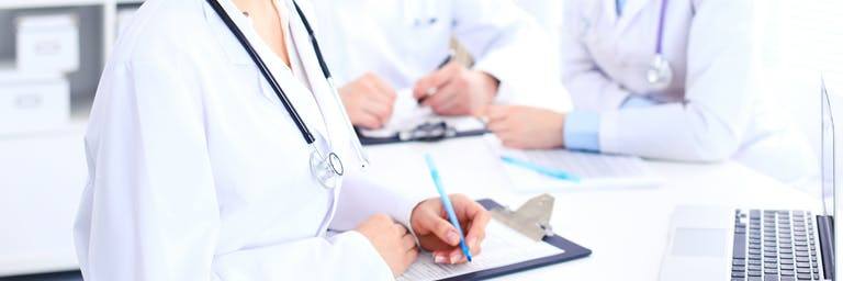 three doctors having a meeting and writing notes around a white table